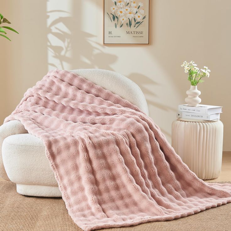 a pink blanket sitting on top of a white chair next to a vase with flowers