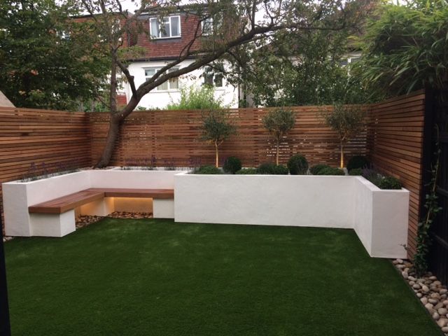 a small backyard with grass and wooden fenced in area, including a built in bench