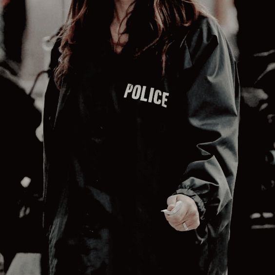 a woman with long hair wearing a police jacket and pointing her finger at the camera