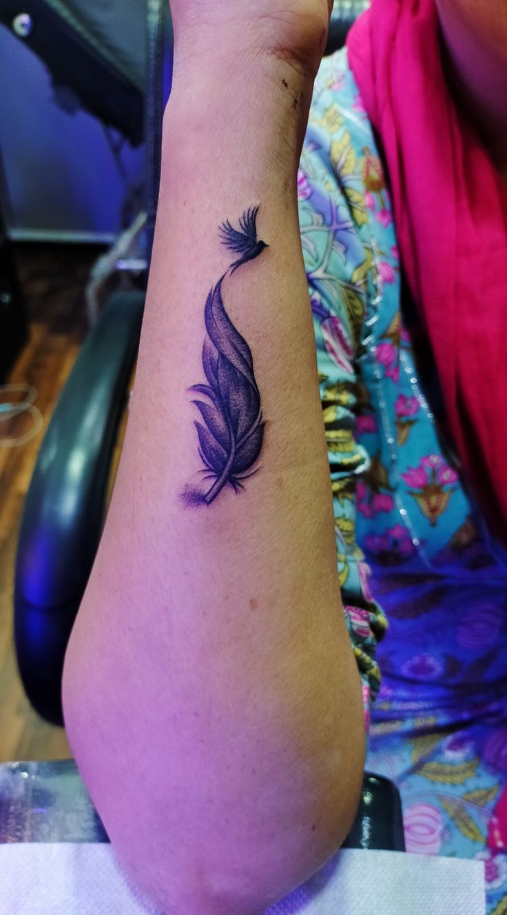 a woman's arm with a tattoo on it that has a purple and black feather