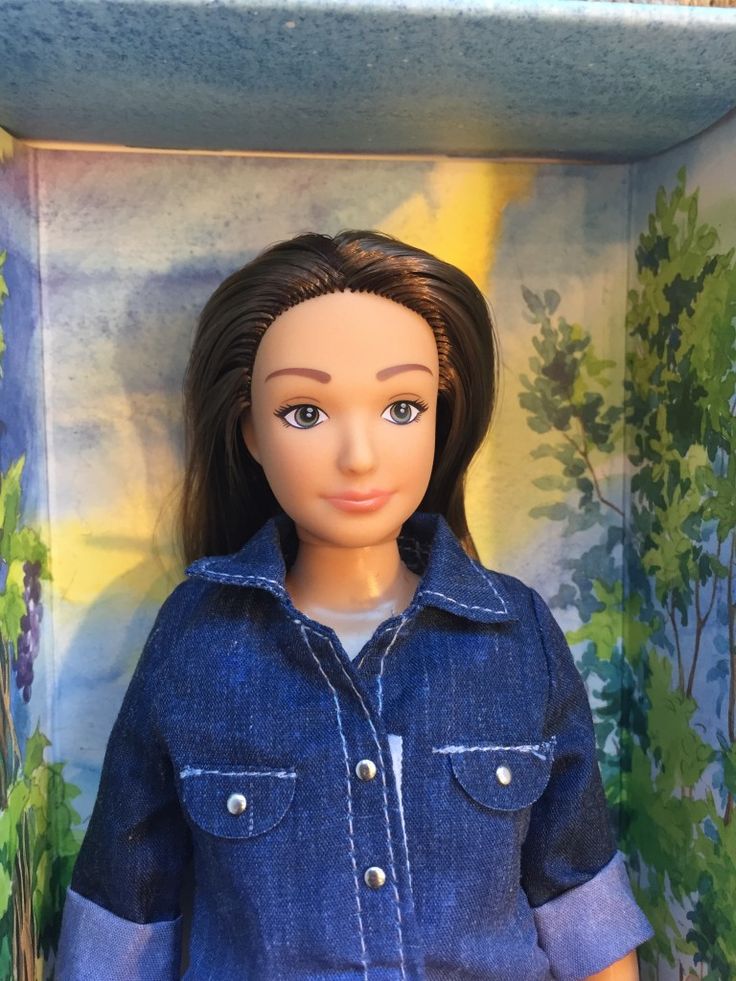 a doll in a box with trees on the wall behind it and a blue denim jacket