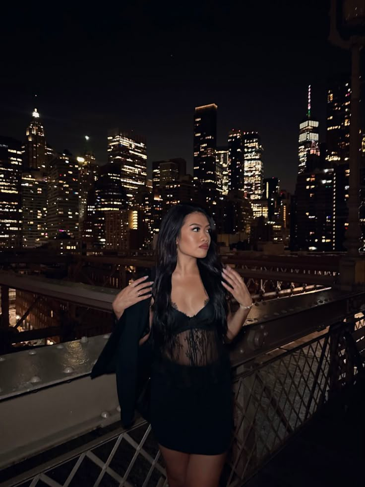 a woman standing on top of a bridge in front of a city skyline at night