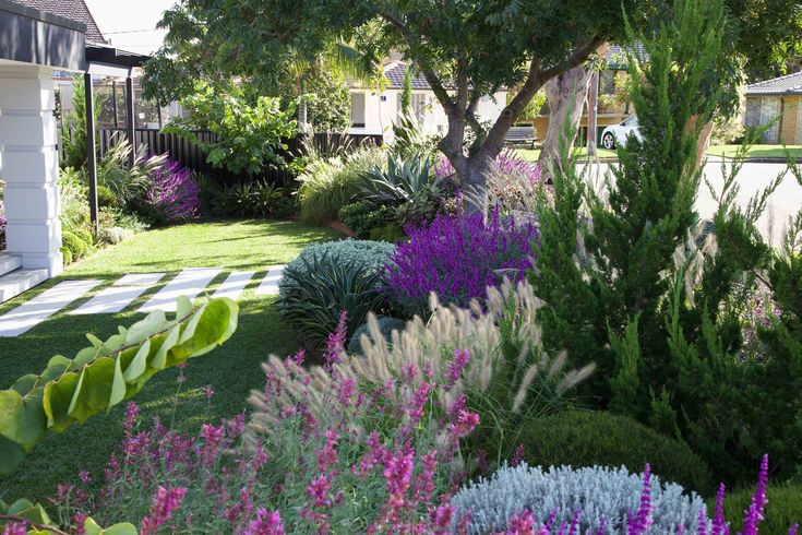 a garden filled with lots of purple and white flowers next to a house in the background