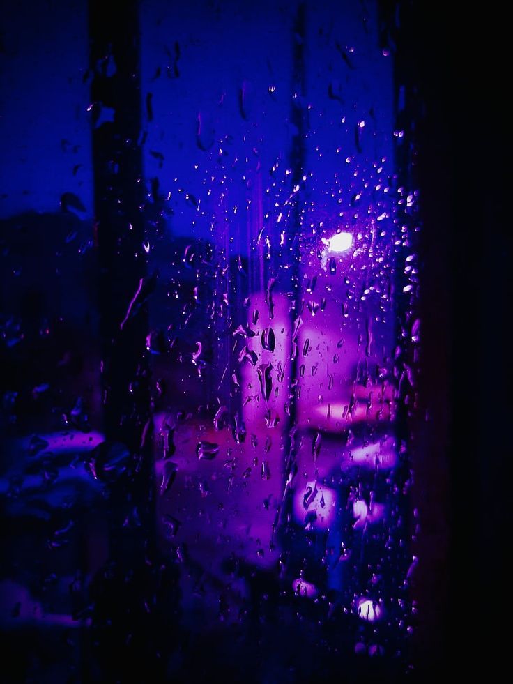 rain drops on the window as it sits in front of a purple building at night