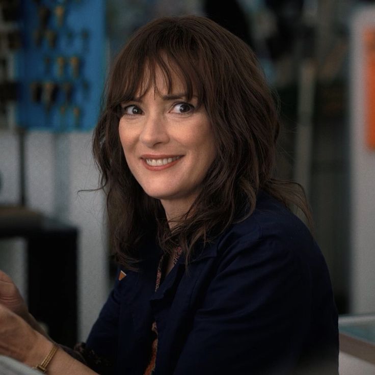 a woman sitting at a table with a glass of wine in her hand and smiling