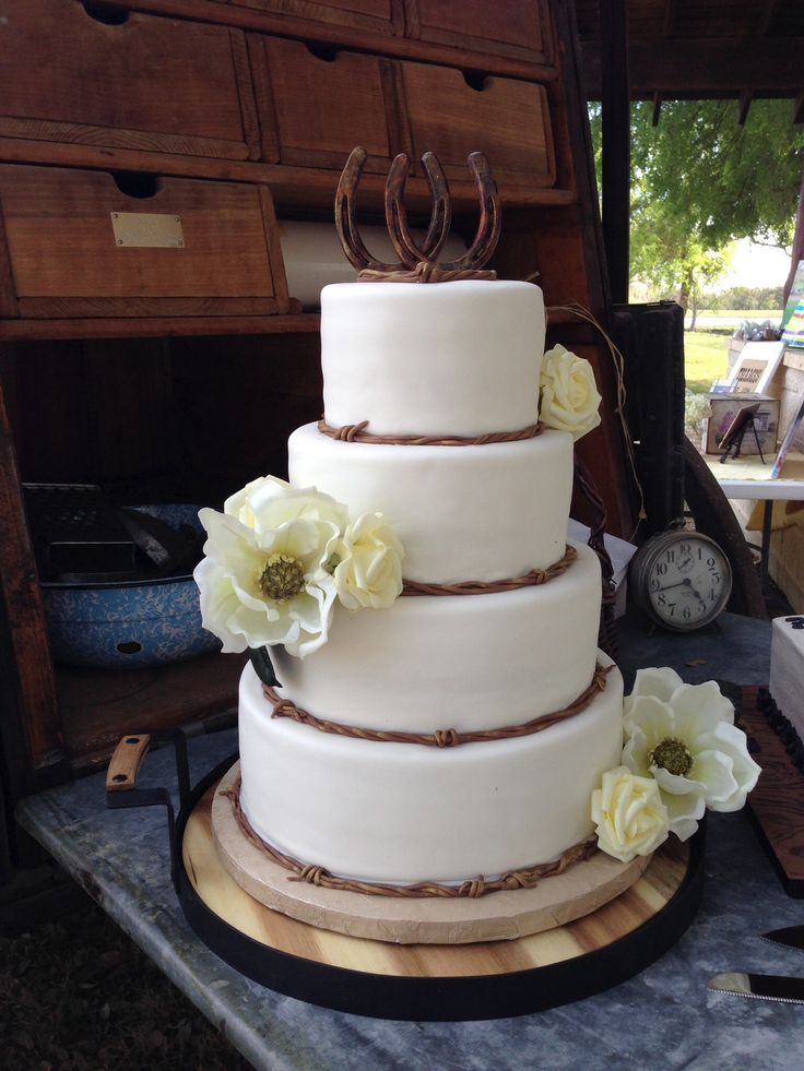 a three tiered cake with white flowers on a wooden table next to a clock