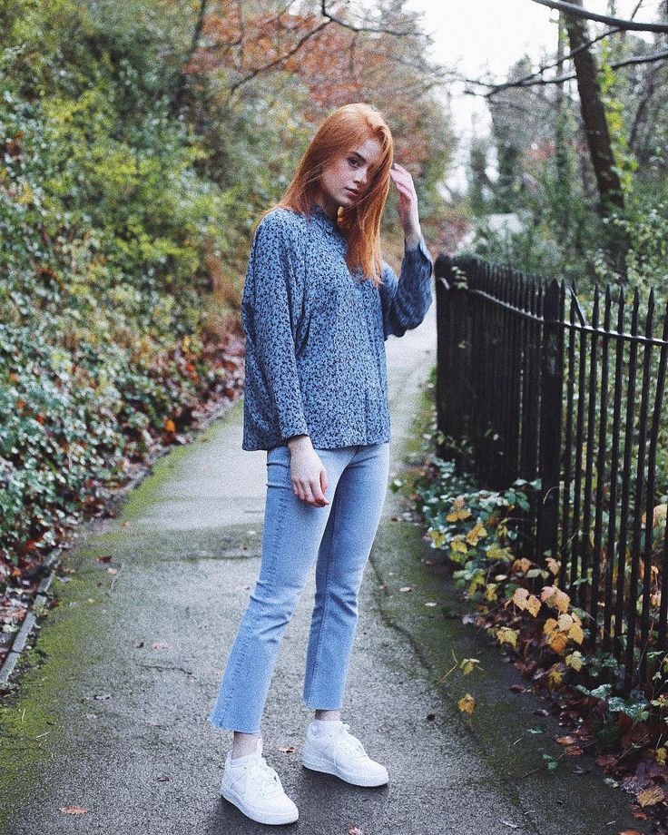 a woman with red hair is standing on the sidewalk wearing jeans and white tennis shoes