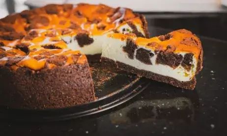 a chocolate cake with orange and white toppings on a black plate next to a slice missing from it