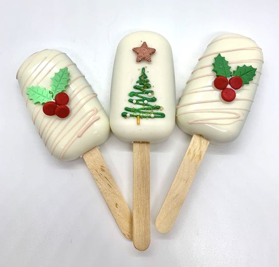 three pops decorated like christmas trees and holly leaves on wooden sticks with white frosting