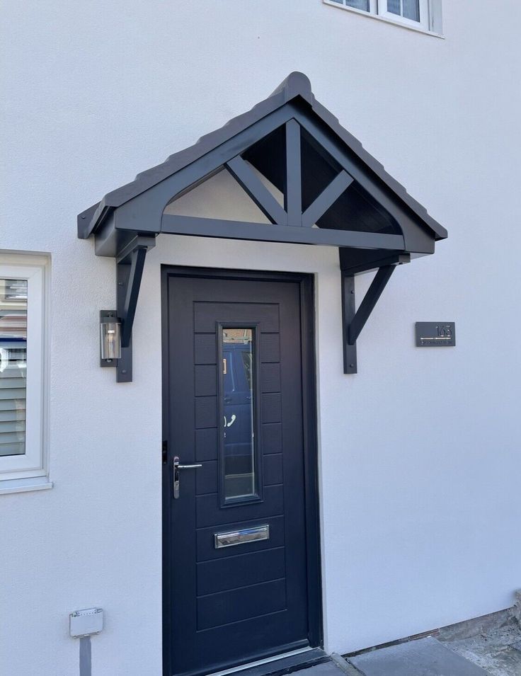 a black door is on the side of a white building with a gray roof and window