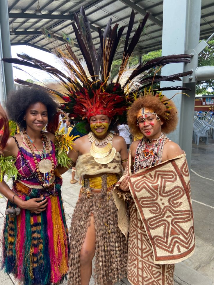 three people dressed in costumes and headdresses posing for the camera at an outdoor event