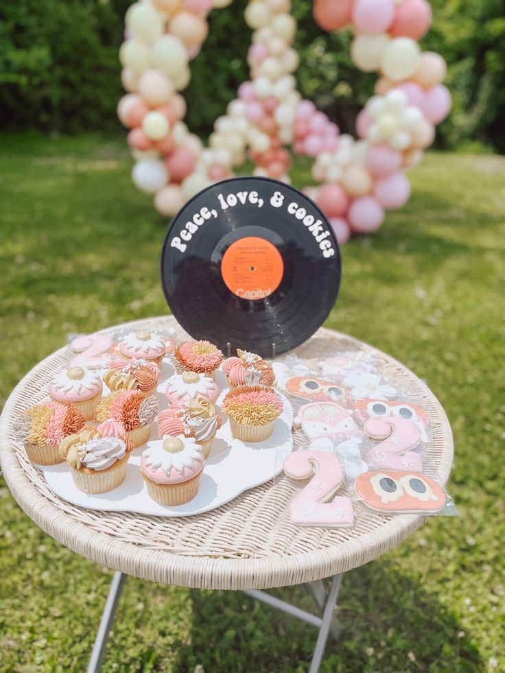 a table topped with cupcakes and cake next to a vinyl record on top of a grass covered field