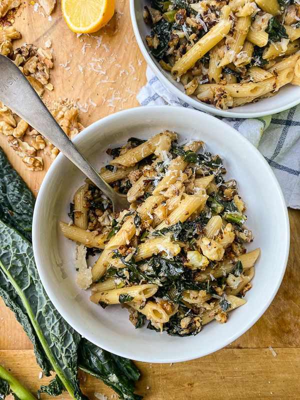 two white bowls filled with pasta and spinach on top of a wooden cutting board