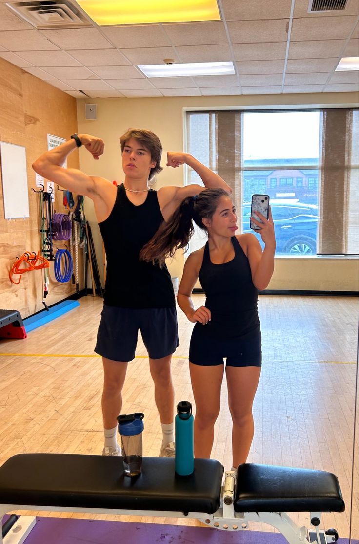 two people standing in a gym with one holding her hair back and the other looking at her cell phone