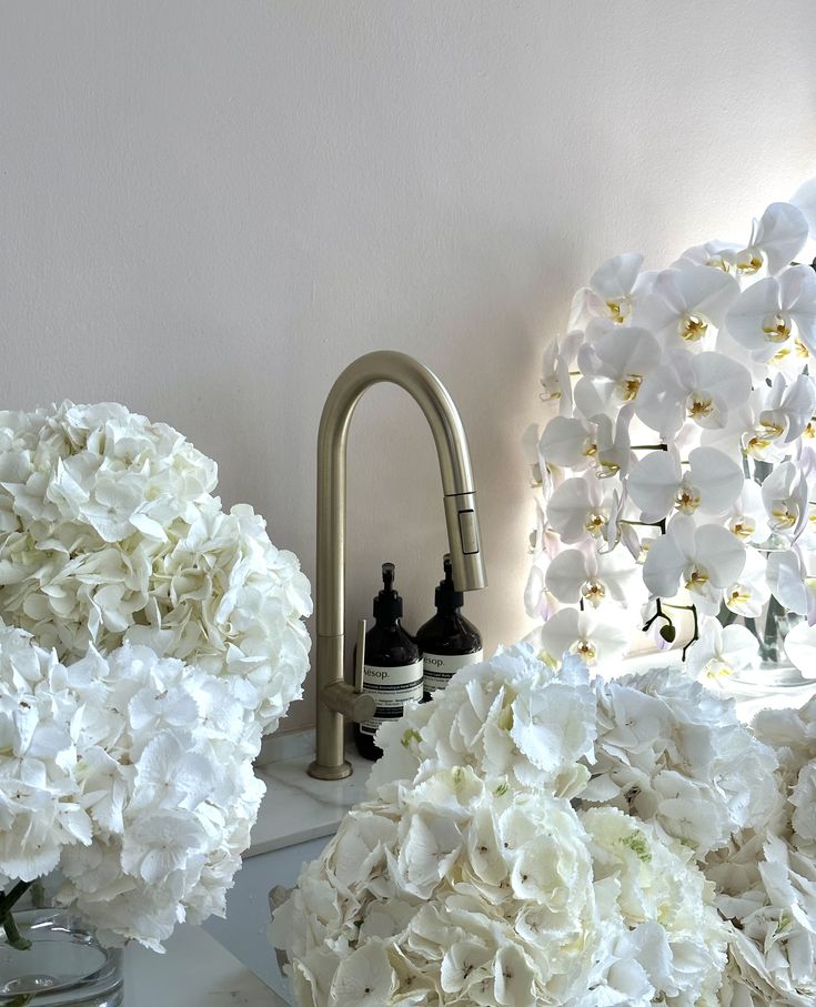 some white flowers are sitting on a table next to a faucet and mirror