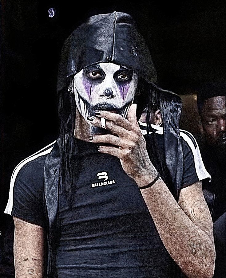 a man with white makeup and black hair is holding a cell phone in his hand