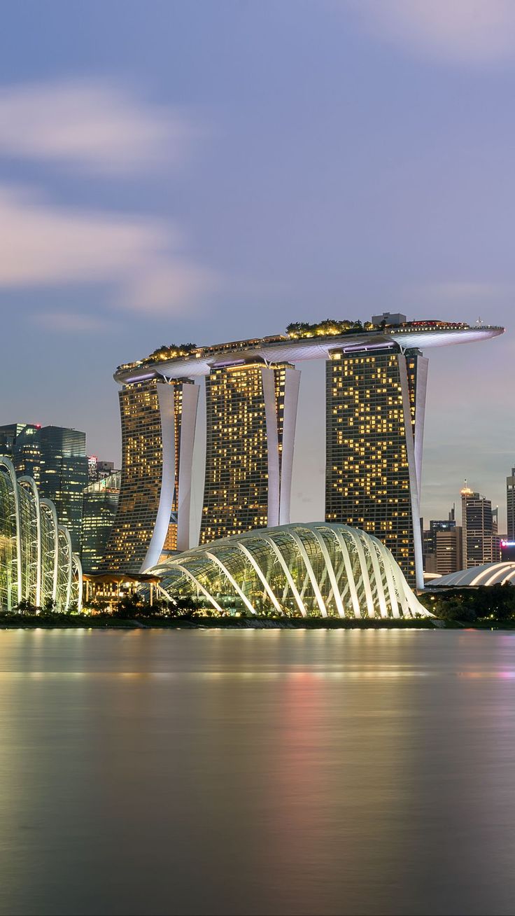 the city skyline is lit up at night with skyscrapers in the foreground and lights reflecting on the water