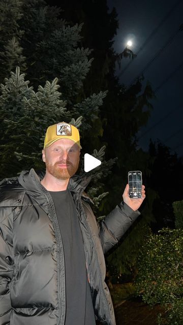 a man wearing a yellow hat and jacket holding a cell phone in his right hand