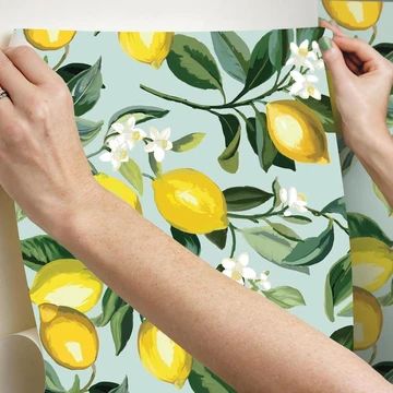 two hands holding up a yellow and white wallpaper with lemons on it