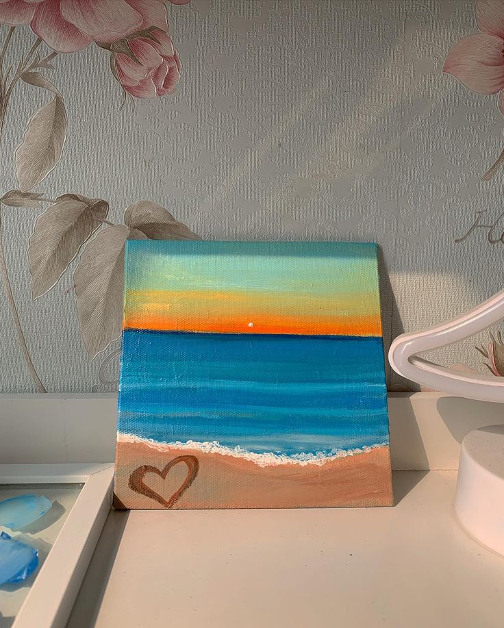 a painting of a heart on the beach next to a vase with flowers and seashells