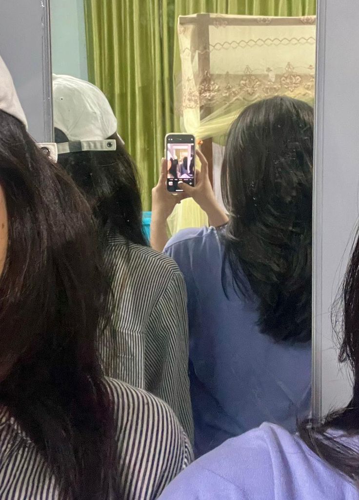 a woman taking a selfie in front of a mirror with other people behind her