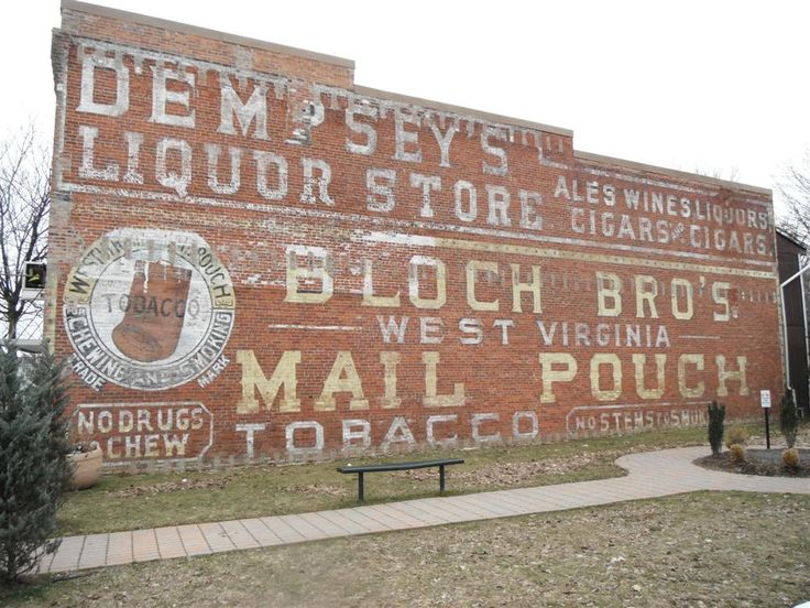 an old brick building with signs painted on it's side and trees in the foreground