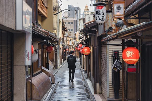 a person walking down an alley way with lanterns hanging from the buildings on both sides