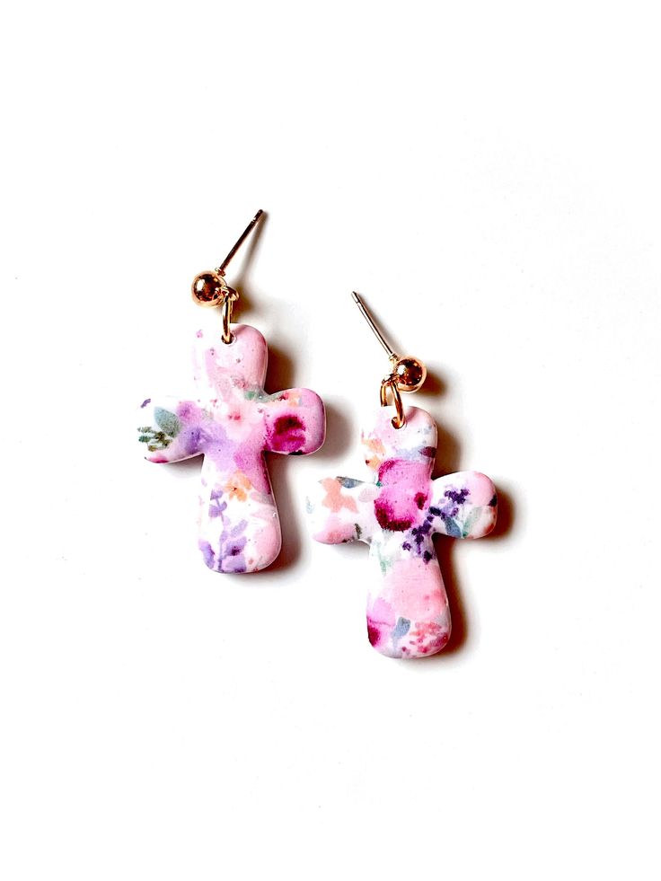 two small pink and purple flowers are hanging from gold ear wires on a white surface