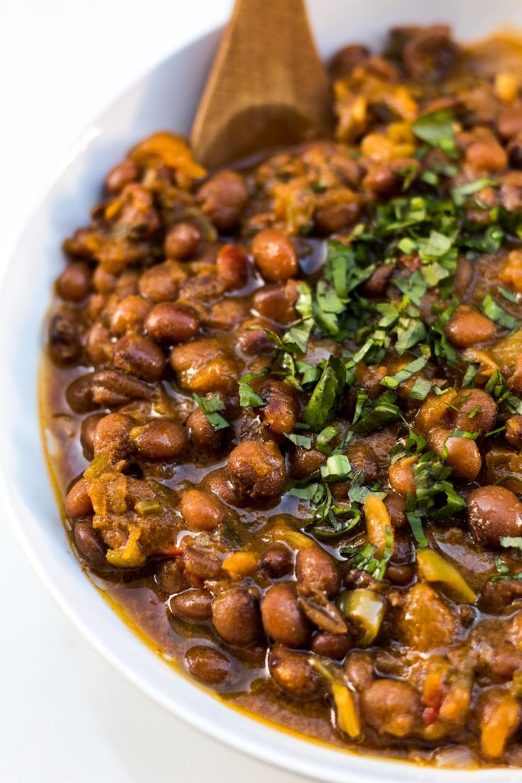 a white bowl filled with beans and greens on top of a table next to a wooden spoon