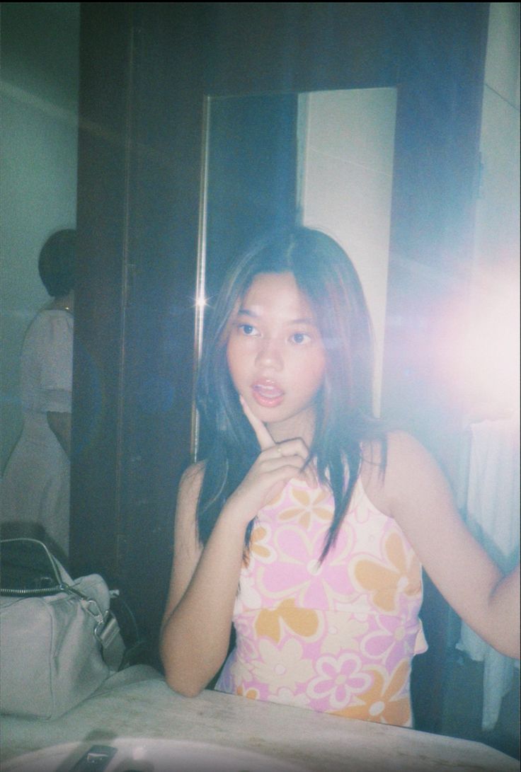 a woman standing in front of a mirror with her hand on her chin and looking at the camera