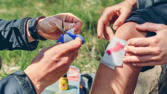 two people sitting on the ground with their feet covered in bandages and one person holding scissors