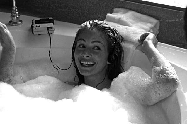 a woman in a bathtub with foam on her head and hair dryer hanging from the ceiling