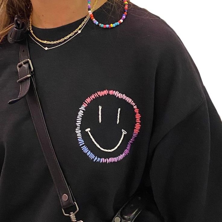 a woman wearing a black sweatshirt with a smiley face on it's chest and colorful beads around her neck