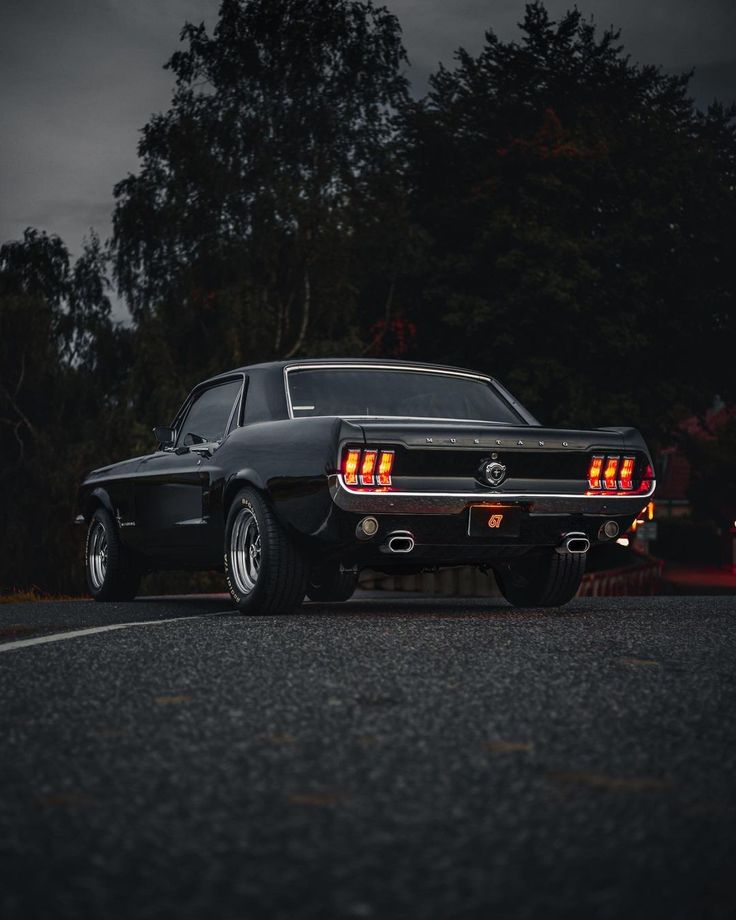 an old black mustang parked on the side of the road