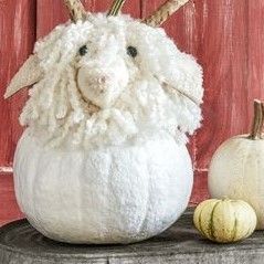 a white stuffed animal sitting on top of a table next to pumpkins and a wooden fence