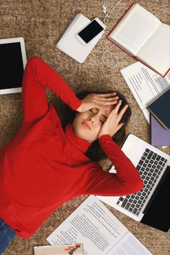 a woman laying on the floor with her head in her hands, surrounded by papers and laptops