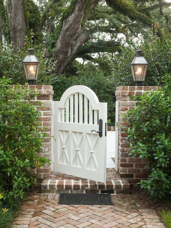 a white gate with two lights on each side and a brick path leading to it