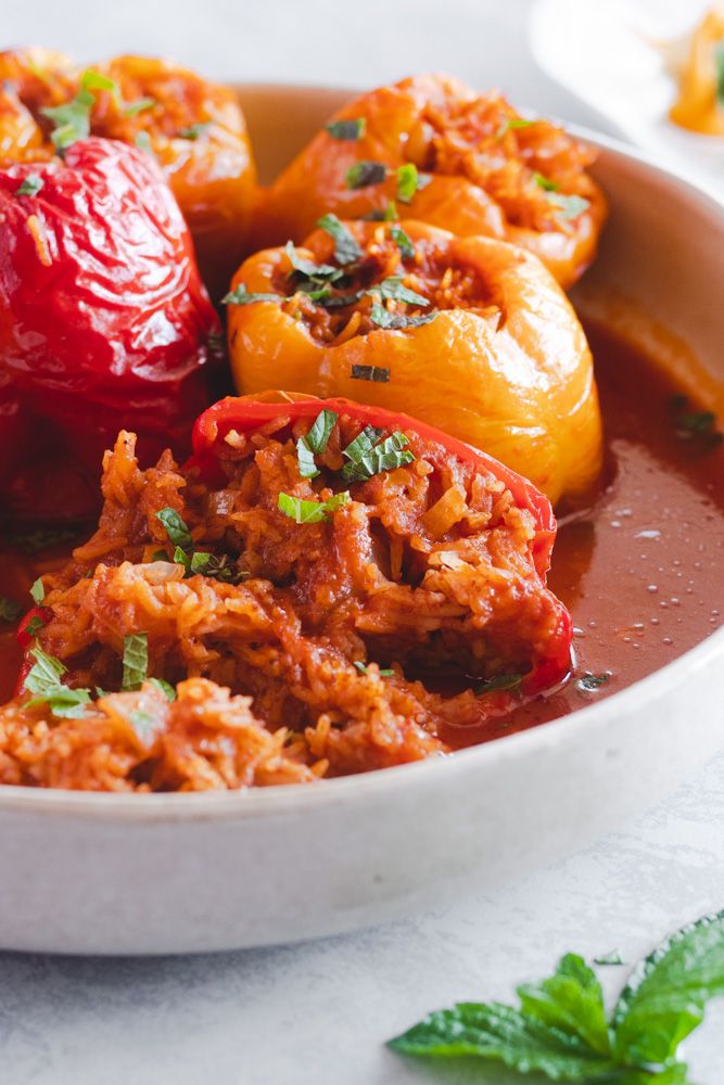 a white bowl filled with red peppers and meat covered in tomato sauce, garnished with parsley