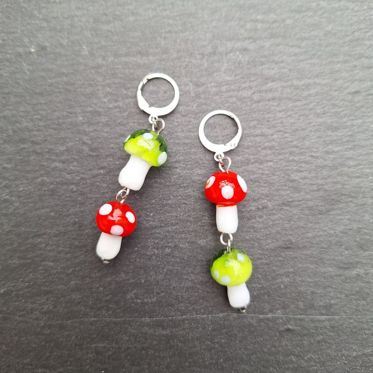 two red and green mushrooms are hanging from silver hoop earrings on a gray table top