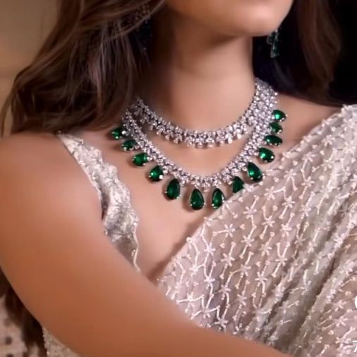 Embrace unmatched sophistication: Inspired by Tara Sutaria's festive sparkle, now yours to shine! Introducing our exquisite jewelry set adorned with shimmering zircons and mesmerizing emerald stones. The look includes a necklace and a pair of earrings. Approximate earrings length is 2". Please click on the video for a detailed view of the product. Silver-plated on high-quality brass as base metal. Made by order. Kindly allow 5-7 weeks for the delivery of this item. For custom or urgent requests, Glamorous Hand Set Jewelry For Celebrations, Glamorous Festive Jewelry For Reception, Luxury Cubic Zirconia Jewelry Sets For Festive Occasion, Dazzling Jewelry Sets For Festive Party, Cubic Zirconia Necklace For Party, May Birthstone, Dazzling American Diamond Necklace For Party, Dazzling American Diamond Jewelry Sets For Party, Celebration Bridal Necklace With Sparkling Stones, Elegant Sparkling Jewelry For Festive Occasions