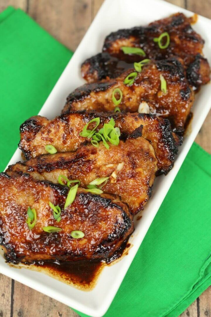 grilled chicken on a white plate with green garnishes and seasoning