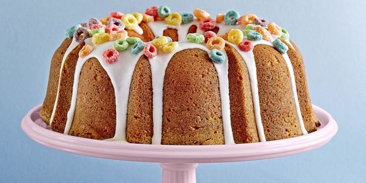 a bundt cake with white icing and colorful cereal toppings on a pink plate