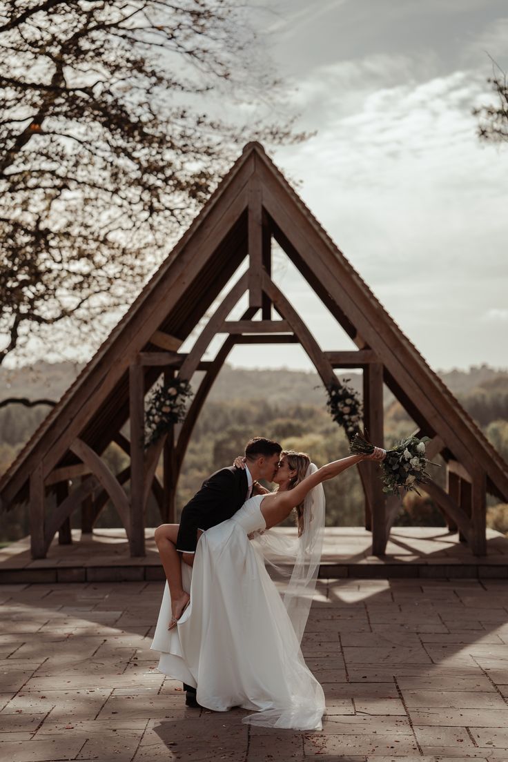 a bride and groom kissing in front of a wooden structure at the end of their wedding day