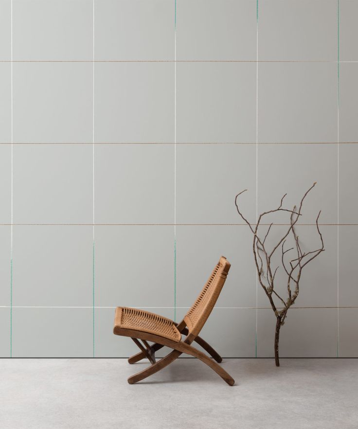 a wooden chair sitting in front of a white tiled wall next to a small tree