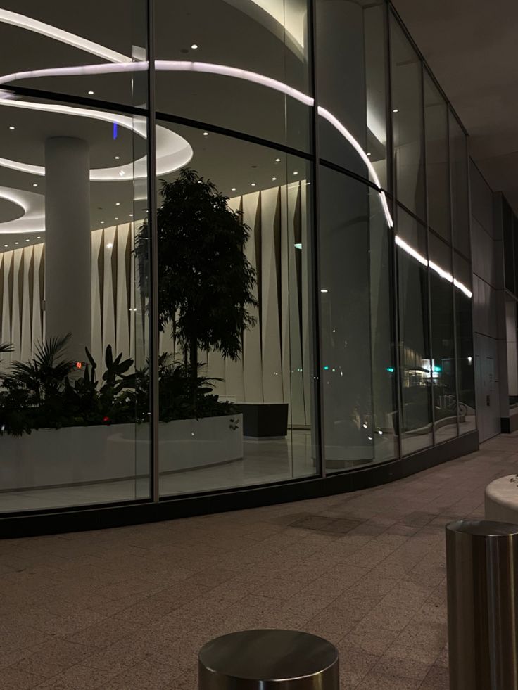 an empty building with large glass windows and plants in the center, at night time