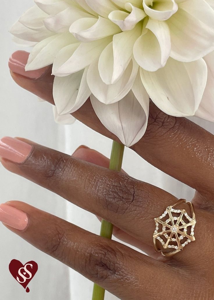 a close up of a person's hand with a ring on it and a flower in the background