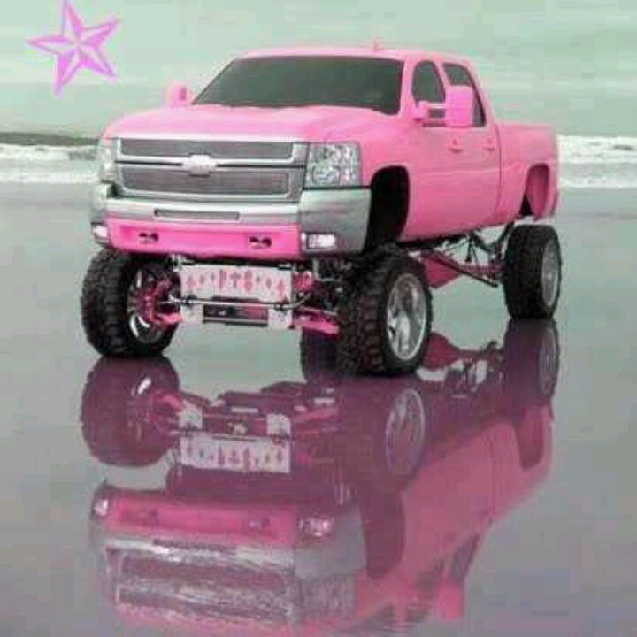 a pink pick up truck is parked on the beach with its reflection in the water