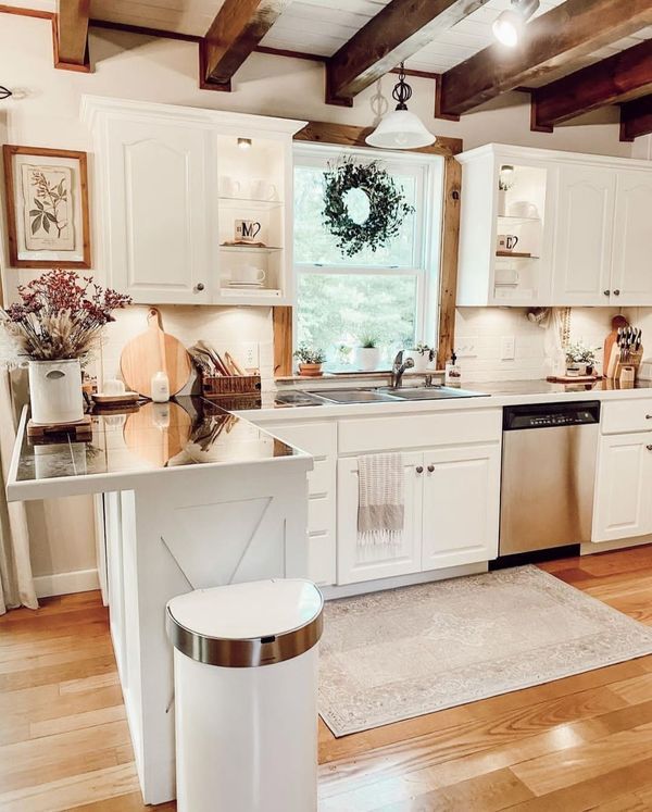 a kitchen with white cabinets and wood floors is pictured in this image, there are wreaths on the window sill