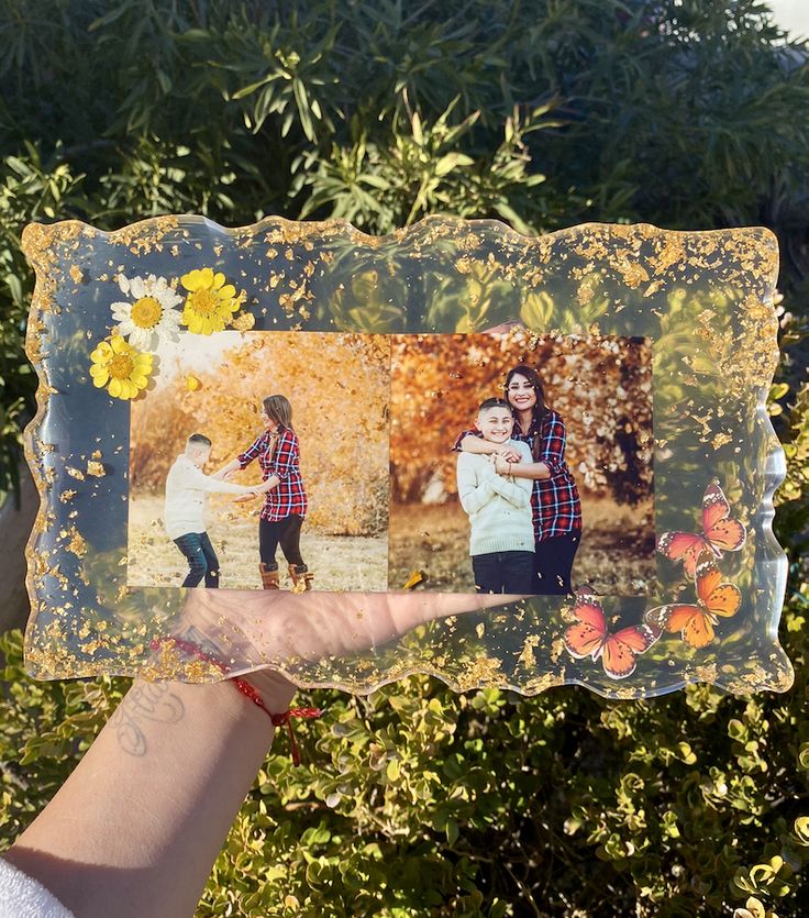 a person holding up an altered photo with flowers and butterflies on it in front of some bushes