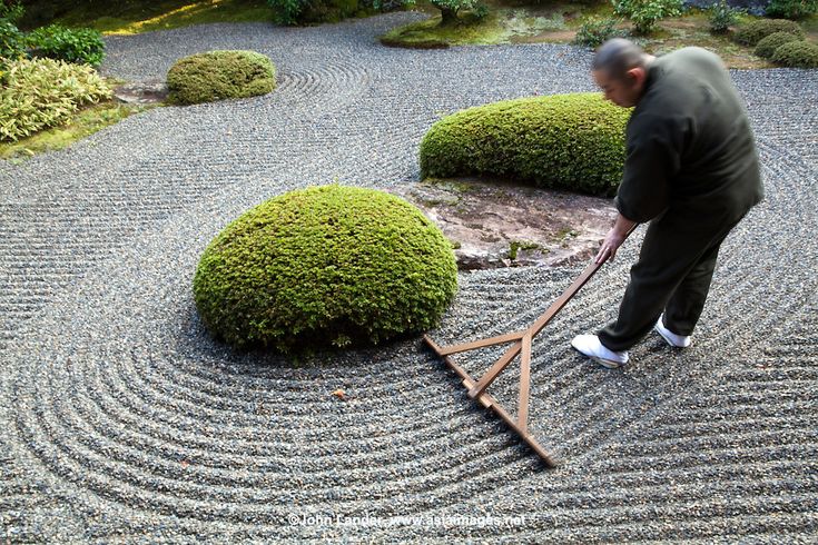 a man is using a wooden rake to cut through the rocks in a japanese garden